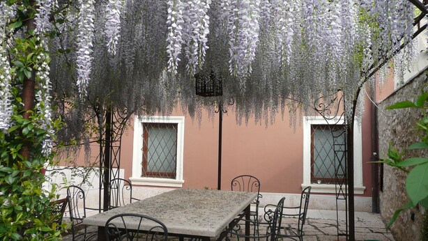 A covered outdoor seating area with a table and chairs, surrounded by a wisteria-covered pergola. - Residence Villa Vinco (Tregnago)