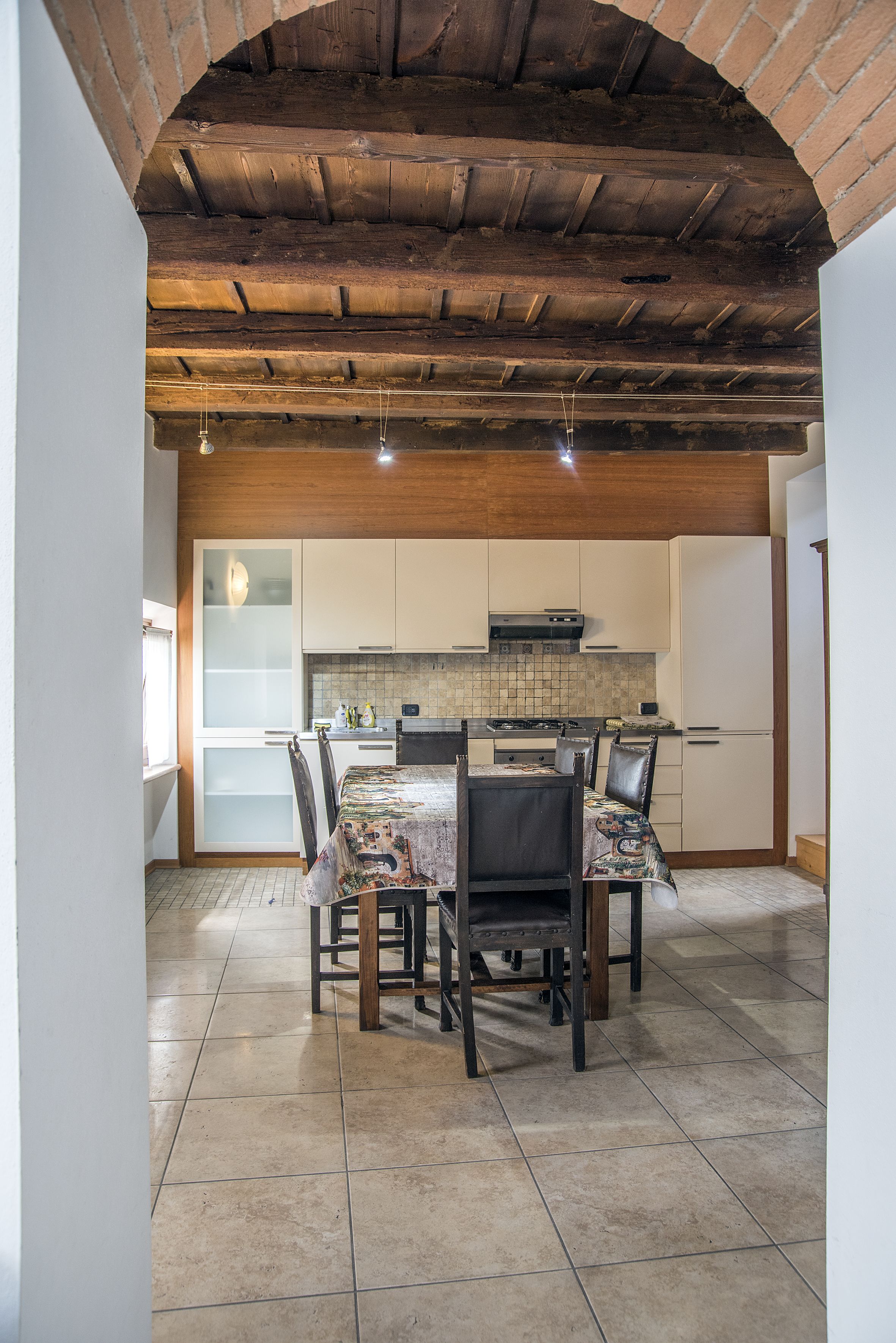 A dining area with a table set for four, a kitchen with white cabinets, and a tiled floor.