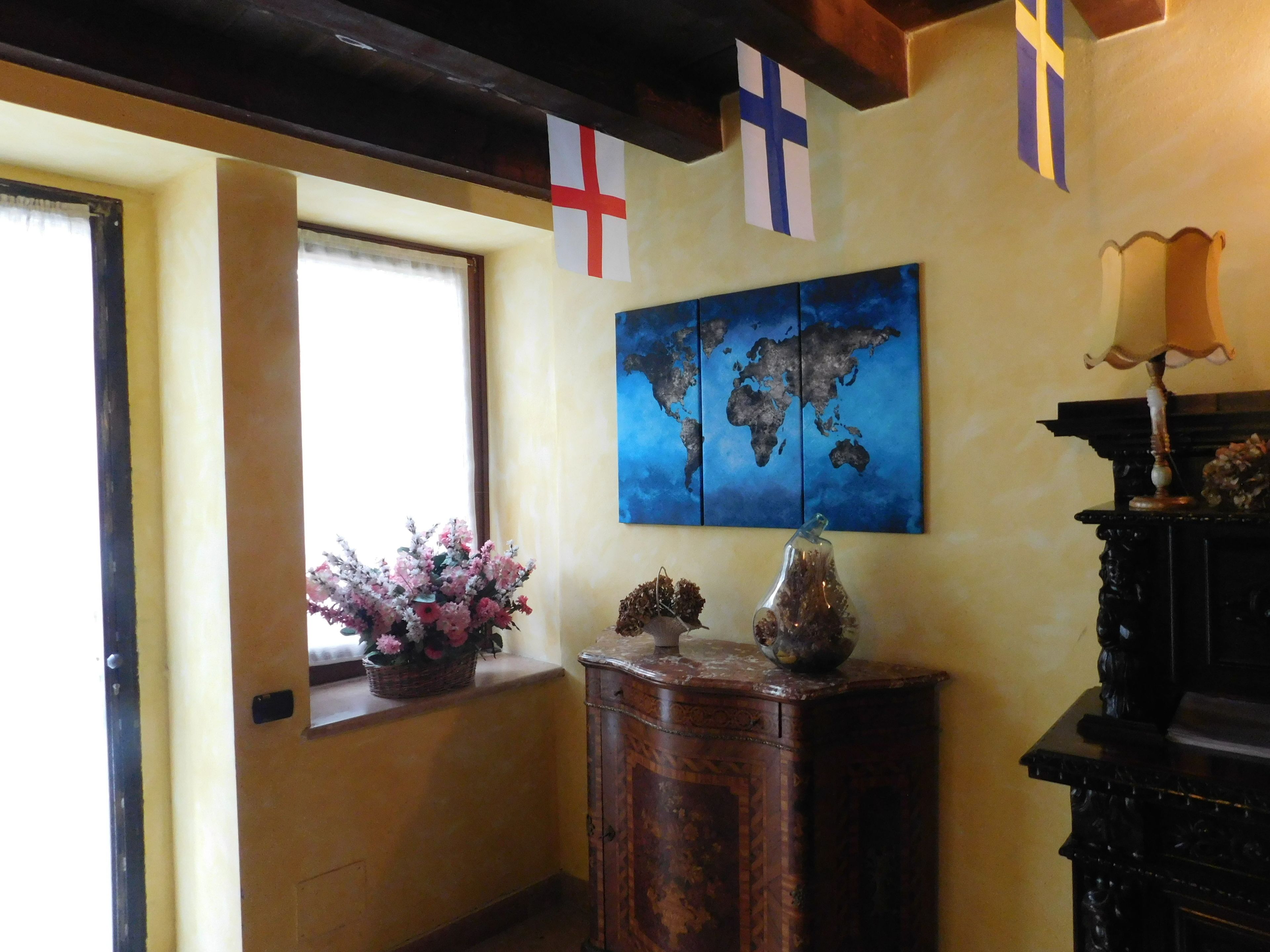 A room with a world map artwork, a window with a view, and a wooden cabinet with decorative items.