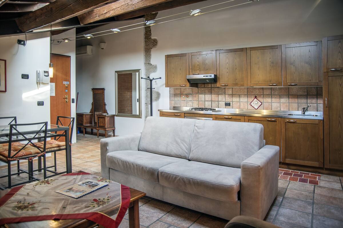 A cozy living area with a sofa, a dining table with chairs, and a kitchen with wooden cabinets and a tiled backsplash.