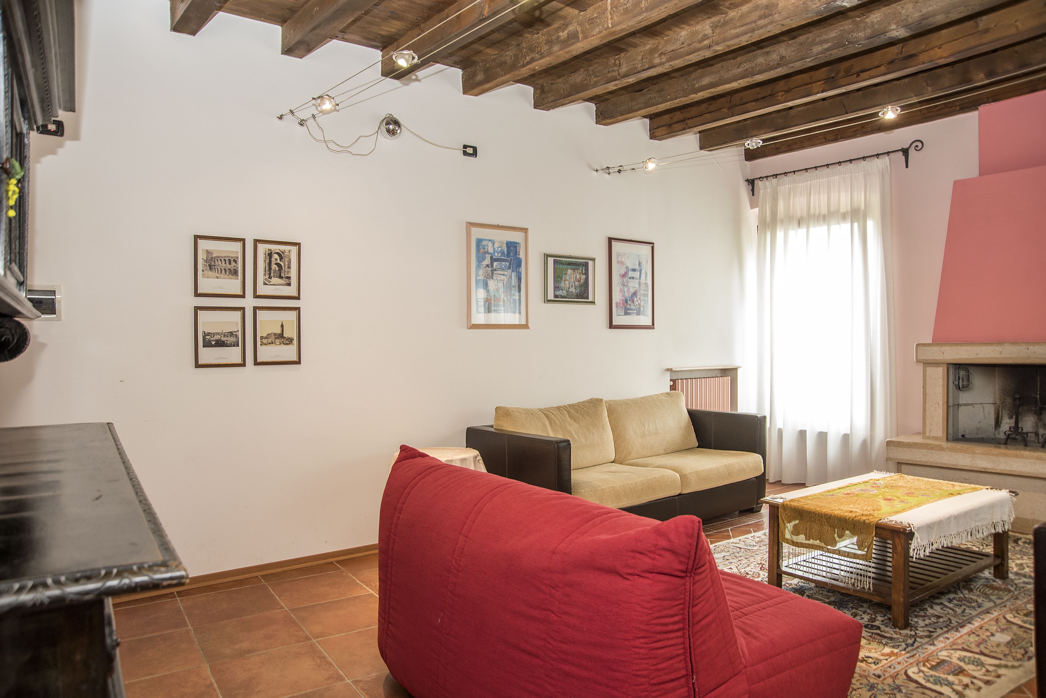 A living room with a sofa, a red chair, a coffee table, and a fireplace. There are framed pictures on the wall.