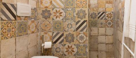Une salle de bain comprenant des toilettes, un espace douche et un mur recouvert de carreaux aux motifs variés.