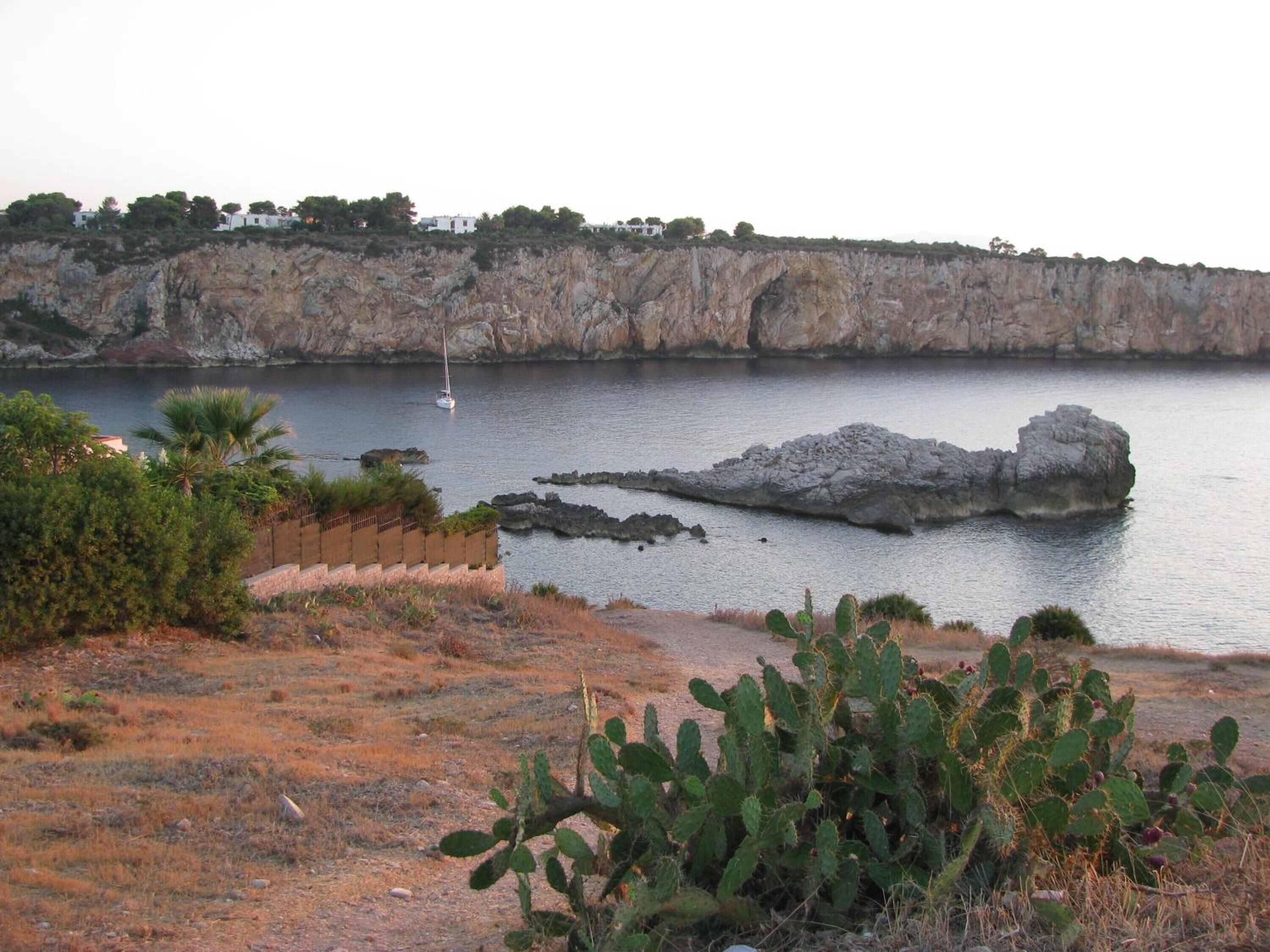 A coastal landscape with a rocky cliff, a small boat, and sparse vegetation including cacti.