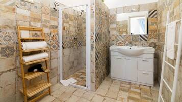 Un baño con ducha, lavamanos y estante de madera con toallas.