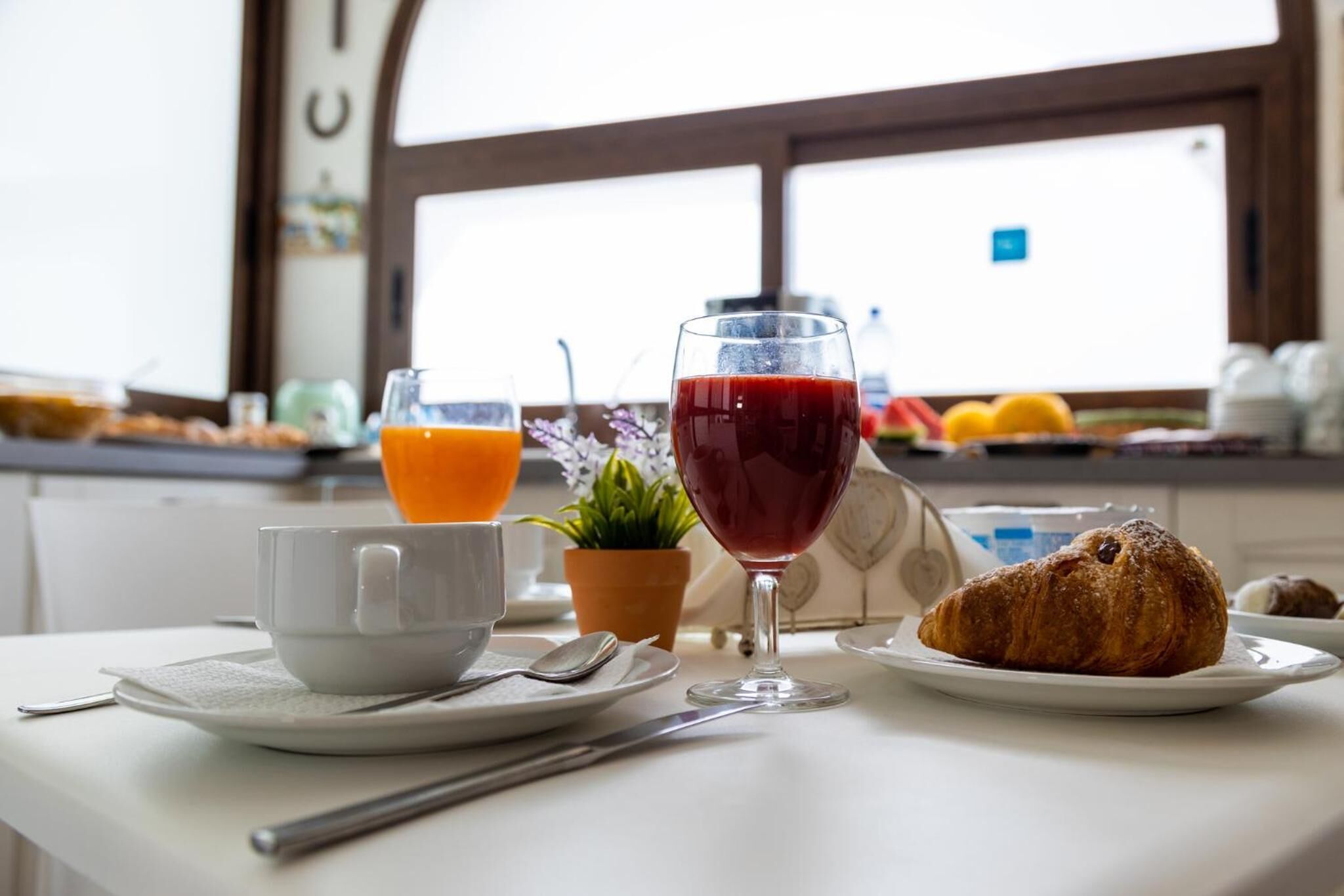 Um ambiente de café da manhã com um croissant, um copo de suco de laranja e um copo de suco vermelho sobre uma mesa.