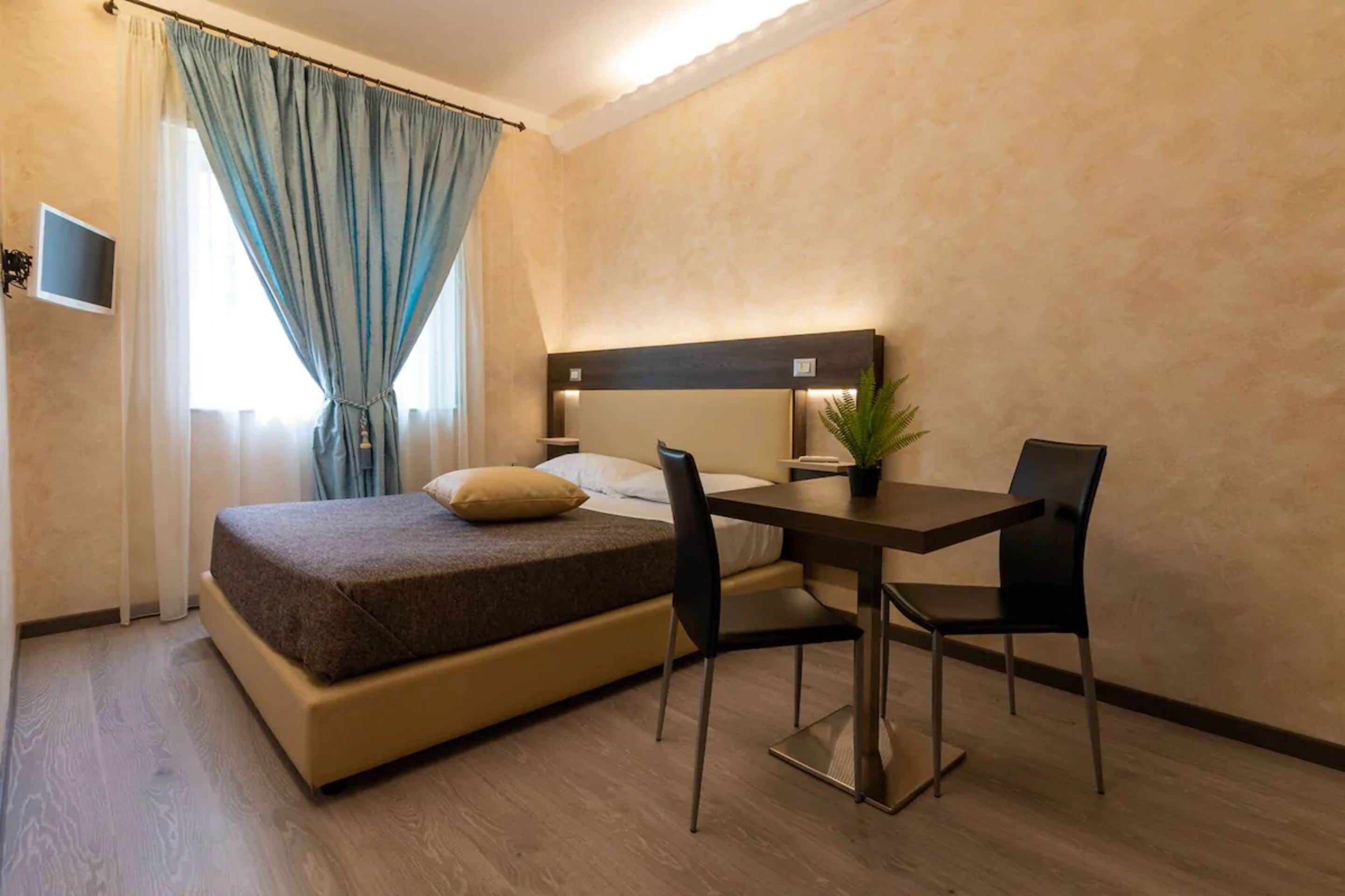 Habitación de hotel con cama, escritorio, dos sillas, televisor y planta en maceta.