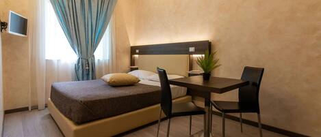Habitación de hotel con cama, escritorio, dos sillas, televisor y planta en maceta.
