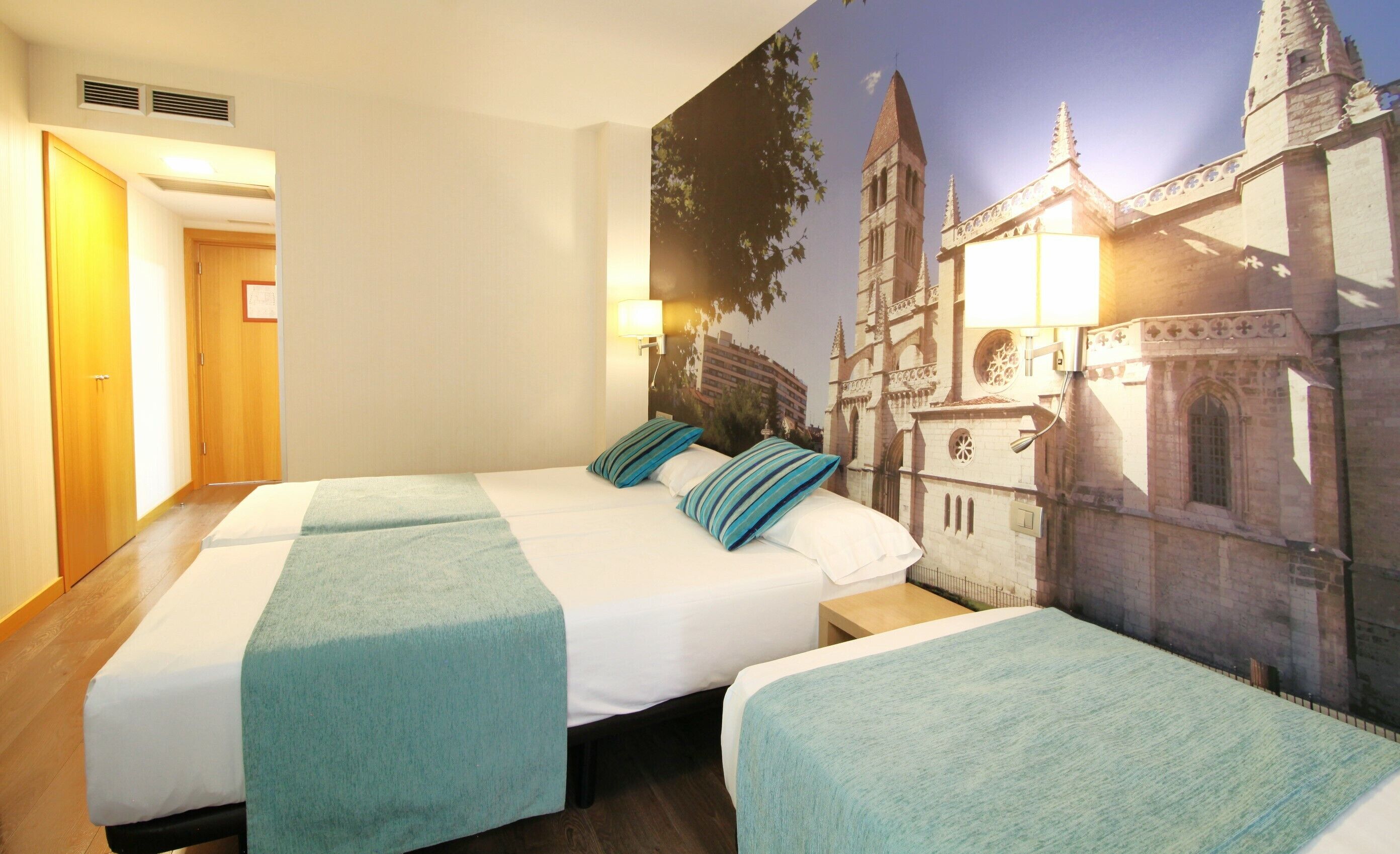 Ein Hotelzimmer mit einem großen Bett, zwei Nachttischen und einem Wandgemälde eines Gebäudes.