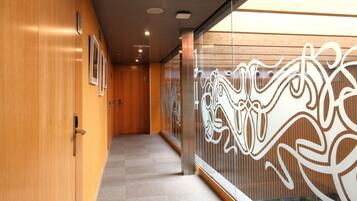 A corridor with wooden walls, a carpeted floor, and a decorative glass partition with abstract patterns.