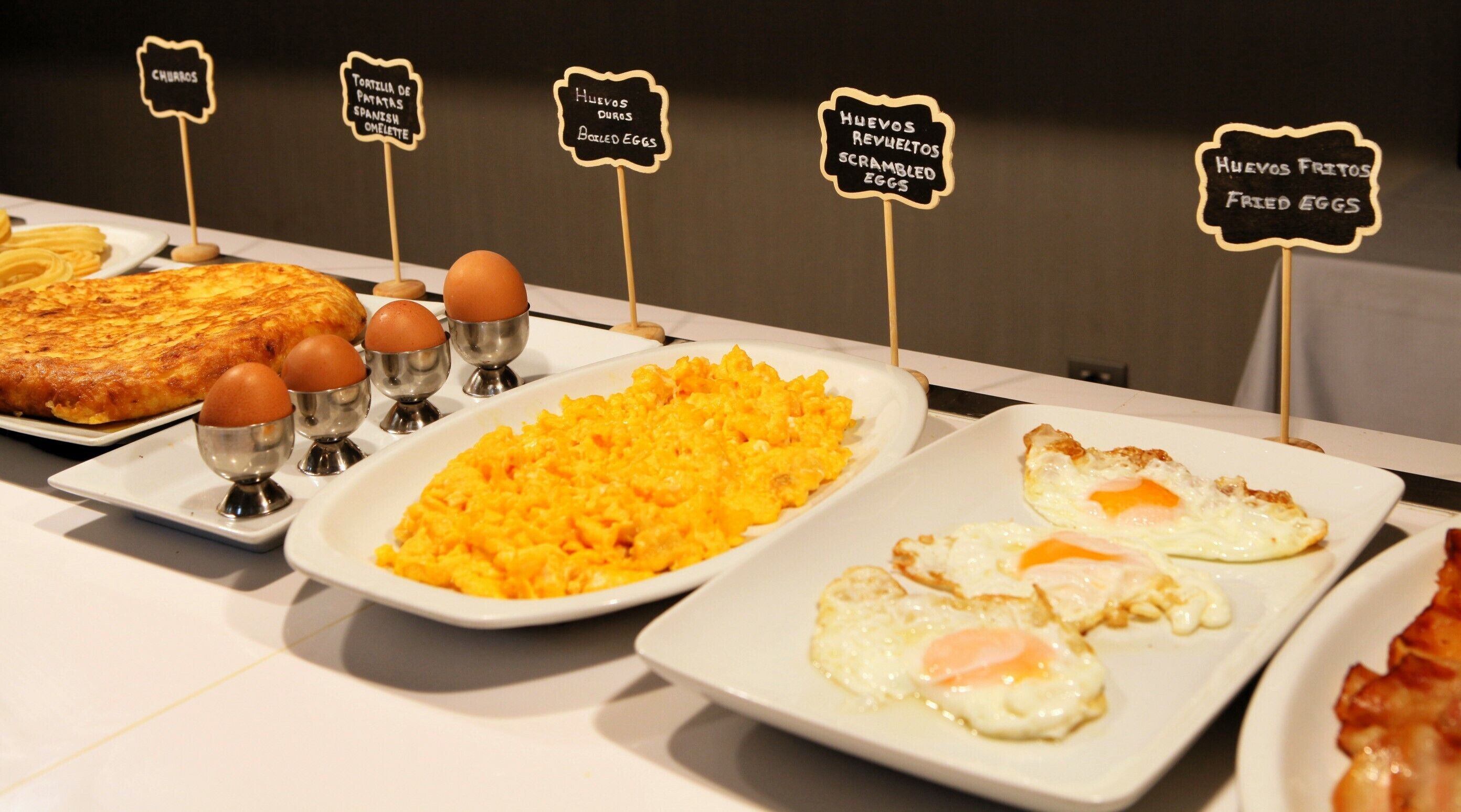 Un bufé de desayuno con una variedad de platos, incluyendo huevos revueltos, huevos benedictinos y una tortilla española.