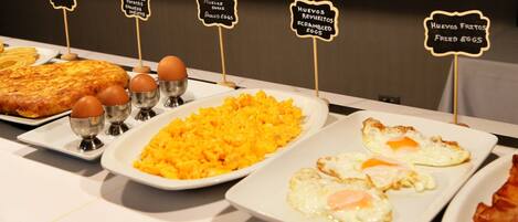 Un bufé de desayuno con una variedad de platos, incluyendo huevos revueltos, huevos benedictinos y una tortilla española.