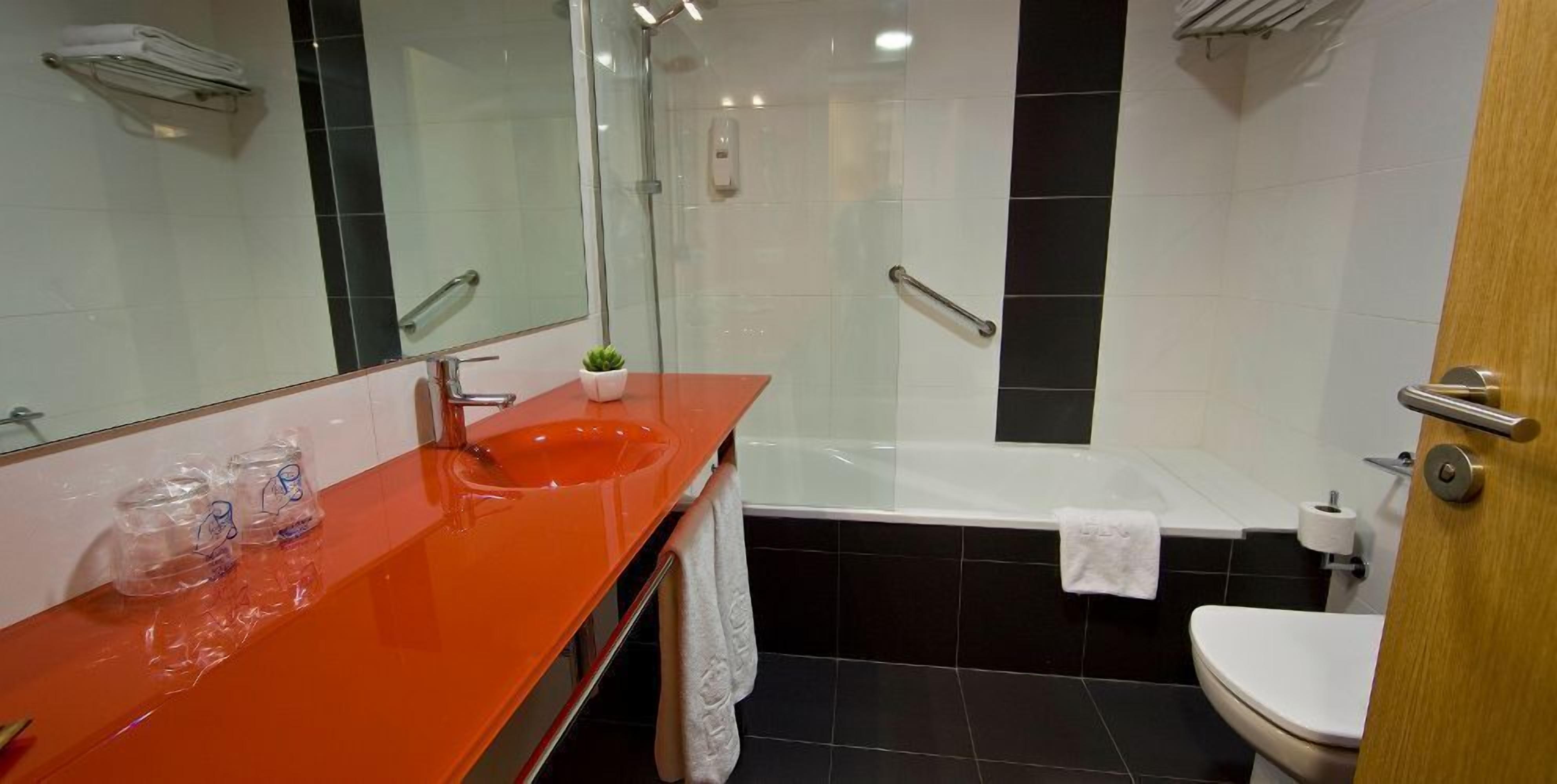 A modern bathroom with a glass-enclosed shower, a red sink, and a white toilet.