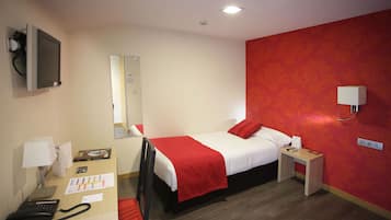 Habitación de hotel con una cama, mesitas de noche, un escritorio con teléfono, una lámpara y un televisor en la pared.