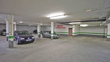 A parking garage with two cars parked, a sign indicating a hotel, and a green and white striped wall.