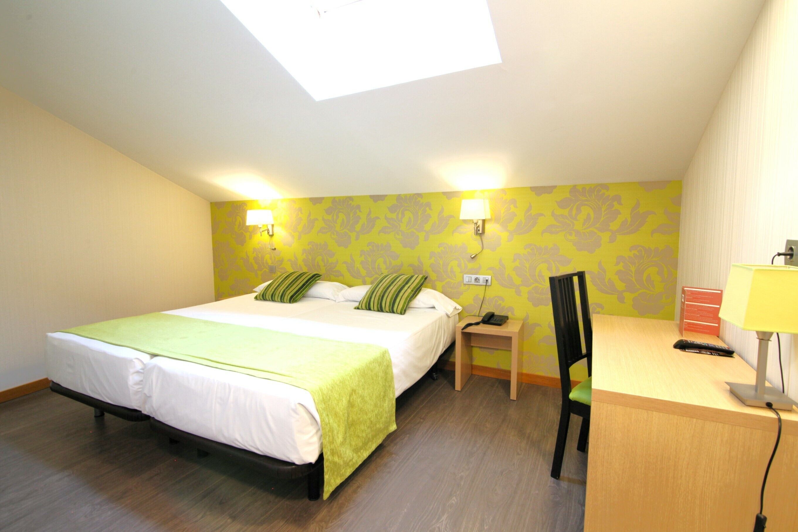 A bedroom with a bed, a desk, a chair, a nightstand, and a lamp.
