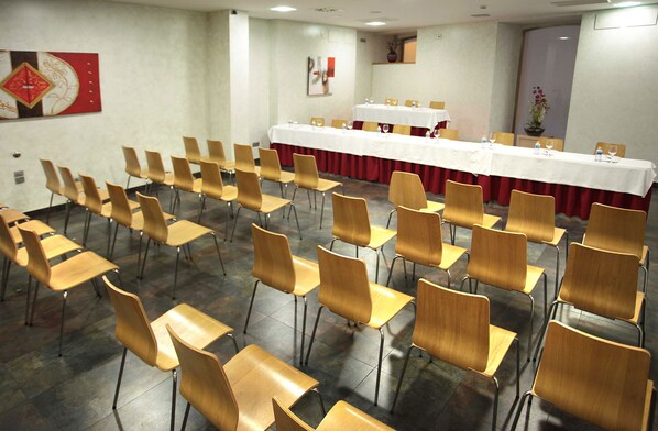 A conference room with rows of wooden chairs, a long table with a white tablecloth, and a red curtain.