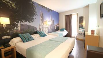 A hotel room with two beds, a desk, a chair, a TV, and a large mural of a cathedral.