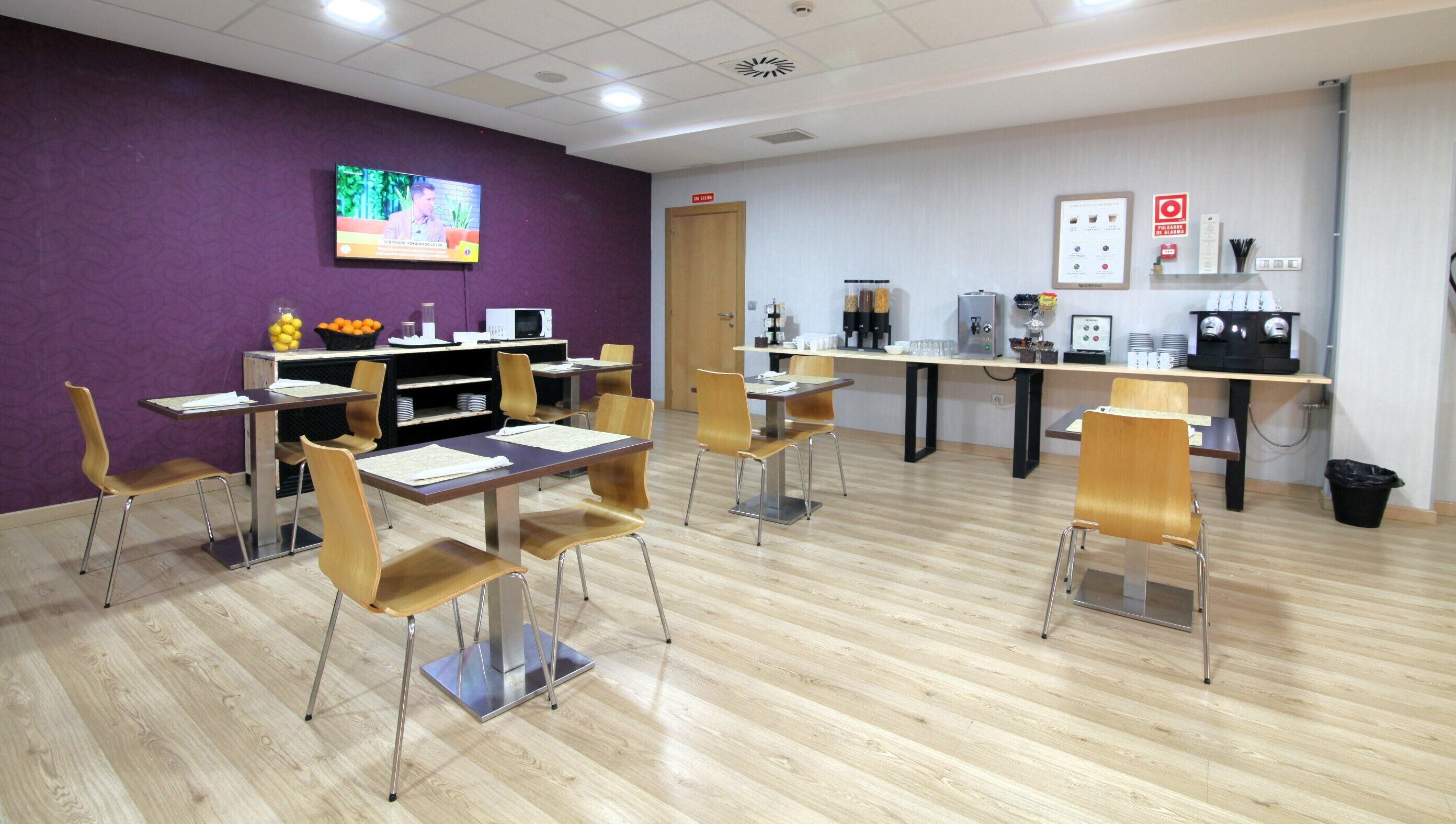 Une salle de conférence moderne, dotée de tables et de chaises en bois, d’un écran de télévision et d’un coin café.