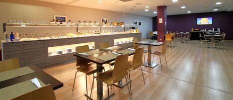 Een moderne eetruimte met een buffetopstelling, tafels, stoelen en een televisiescherm.