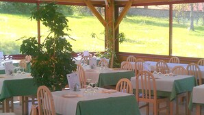 Un restaurante con mesas dispuestas para comer, rodeado de sillas y vistas a un campo verde a través de amplios ventanales.