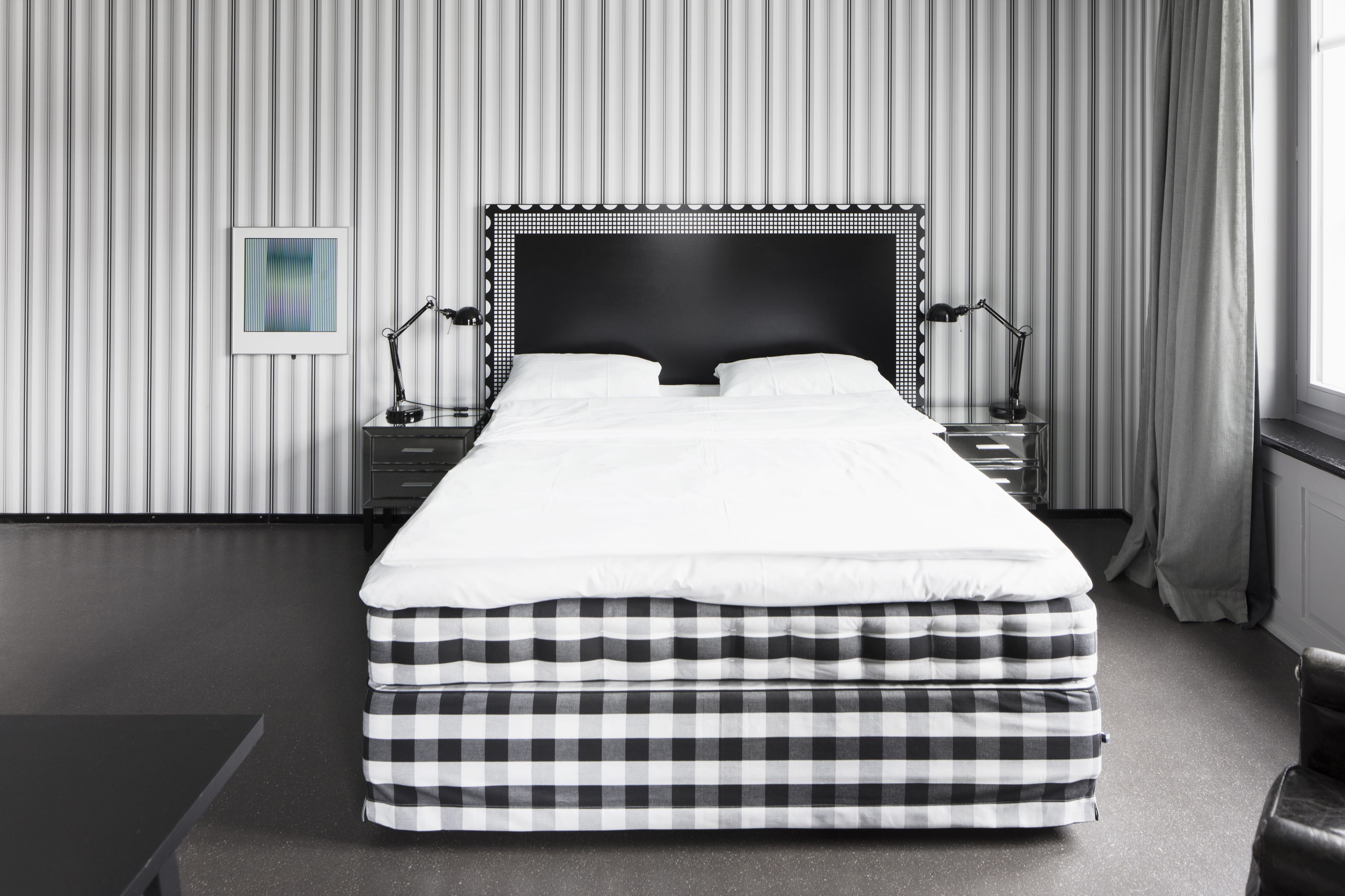 A neatly made bed with a black and white checkered bed skirt, a black headboard, and two bedside lamps.
