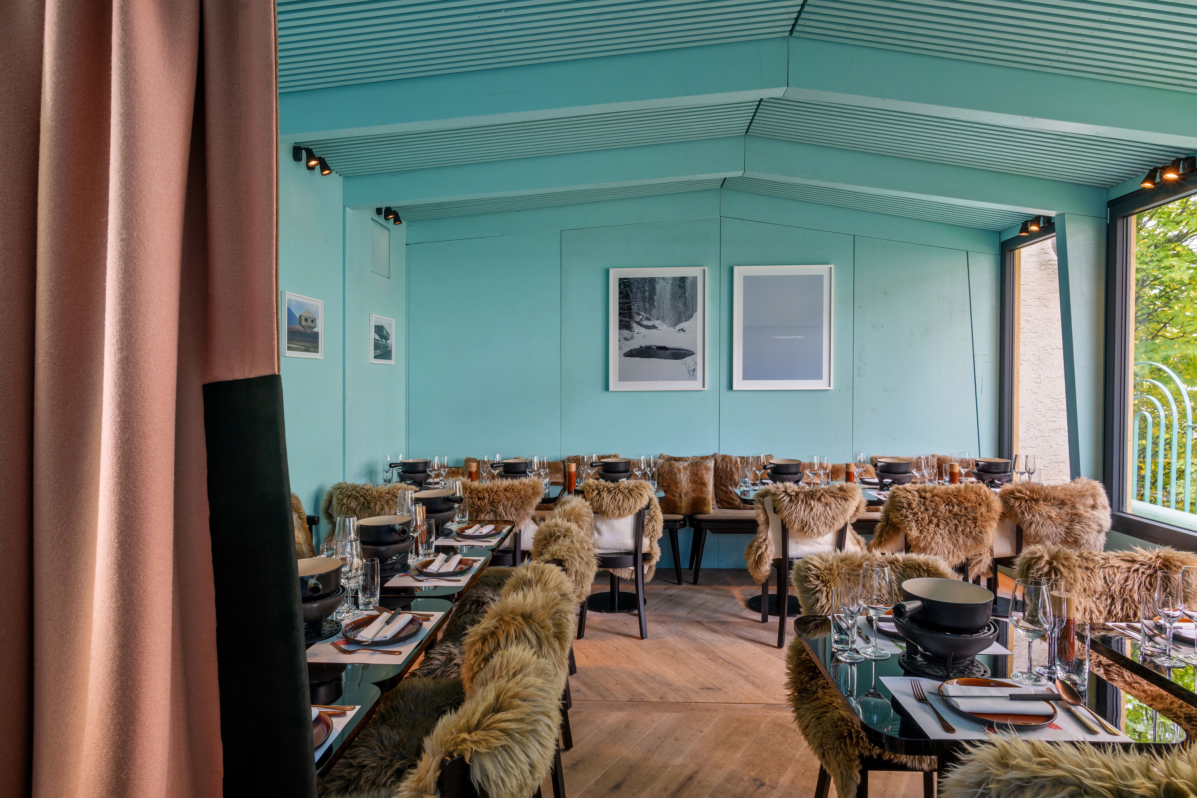 Un restaurante con paredes azul verdoso, piso de madera y sillas cubiertas de piel.