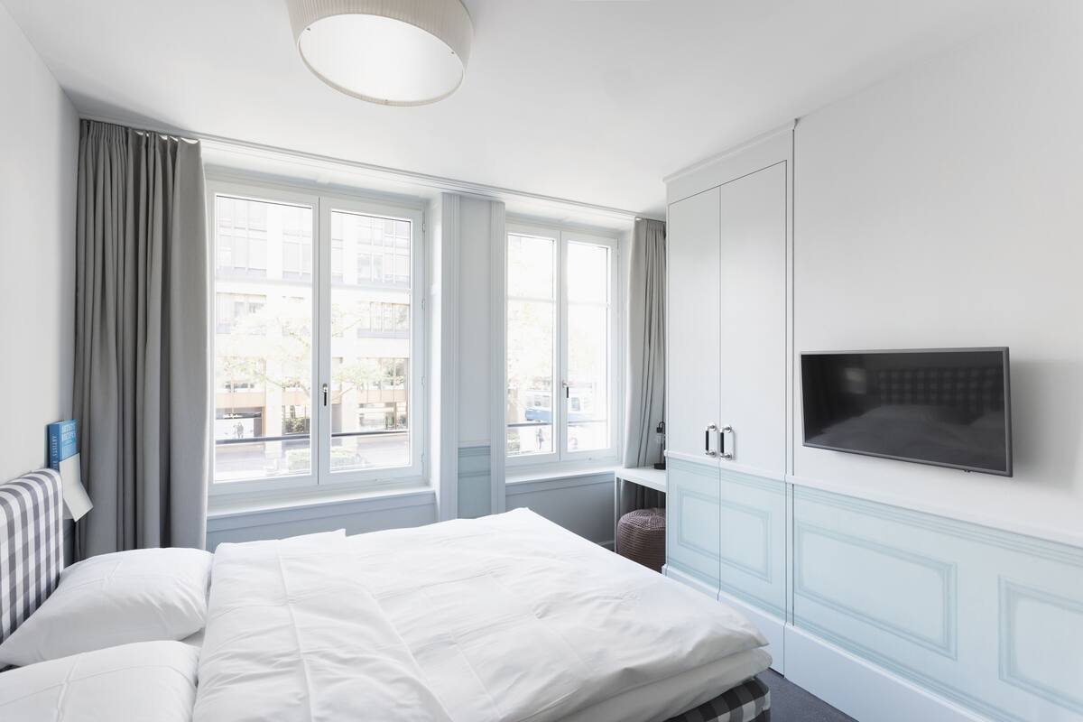 A hotel room with a bed, a TV mounted on the wall, and a window with curtains.