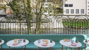 A dining area with round tables set for four, each with pink plates, clear glasses, and cutlery. The tables are placed on a green cushioned bench. - Boutique & Art Hotel Helvetia (Zürich)