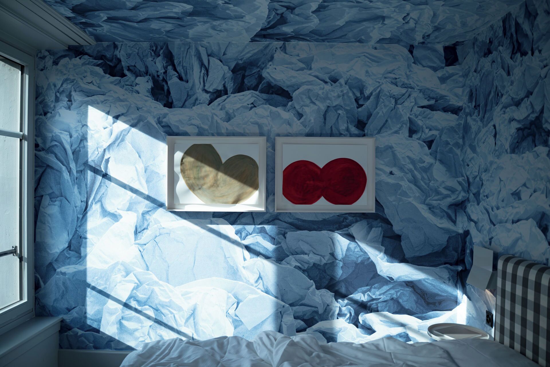 A room with a crumpled fabric wall design, a bed with white bedding, and two framed artworks.