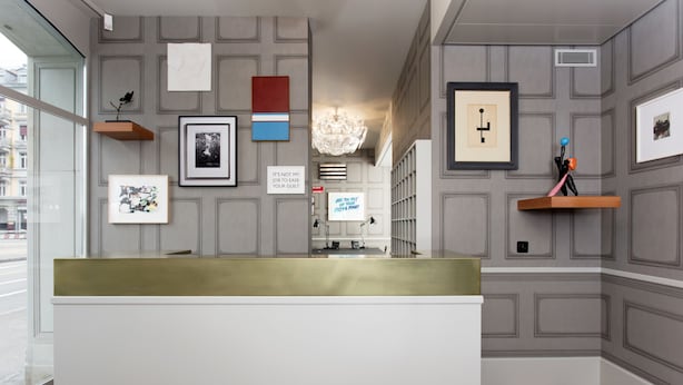A reception area with a white reception desk, framed artwork on the walls, and a chandelier. - Boutique & Art Hotel Helvetia (Zürich)