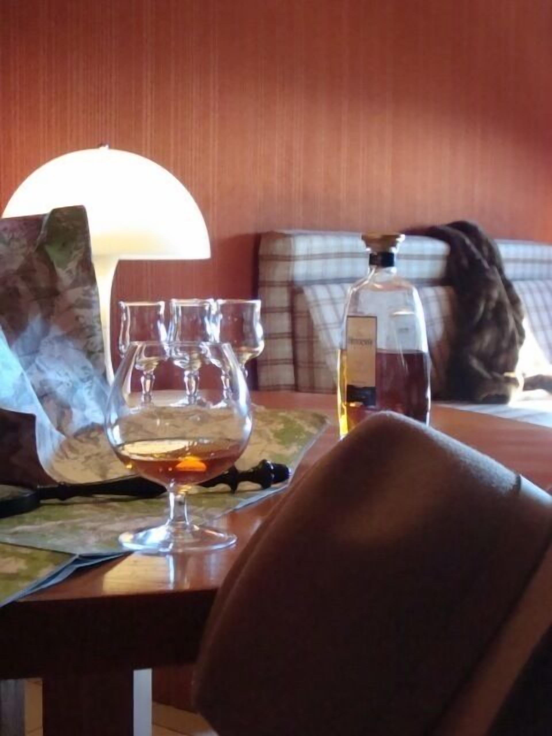 A table with a bottle of liquor, a glass, and a lamp.