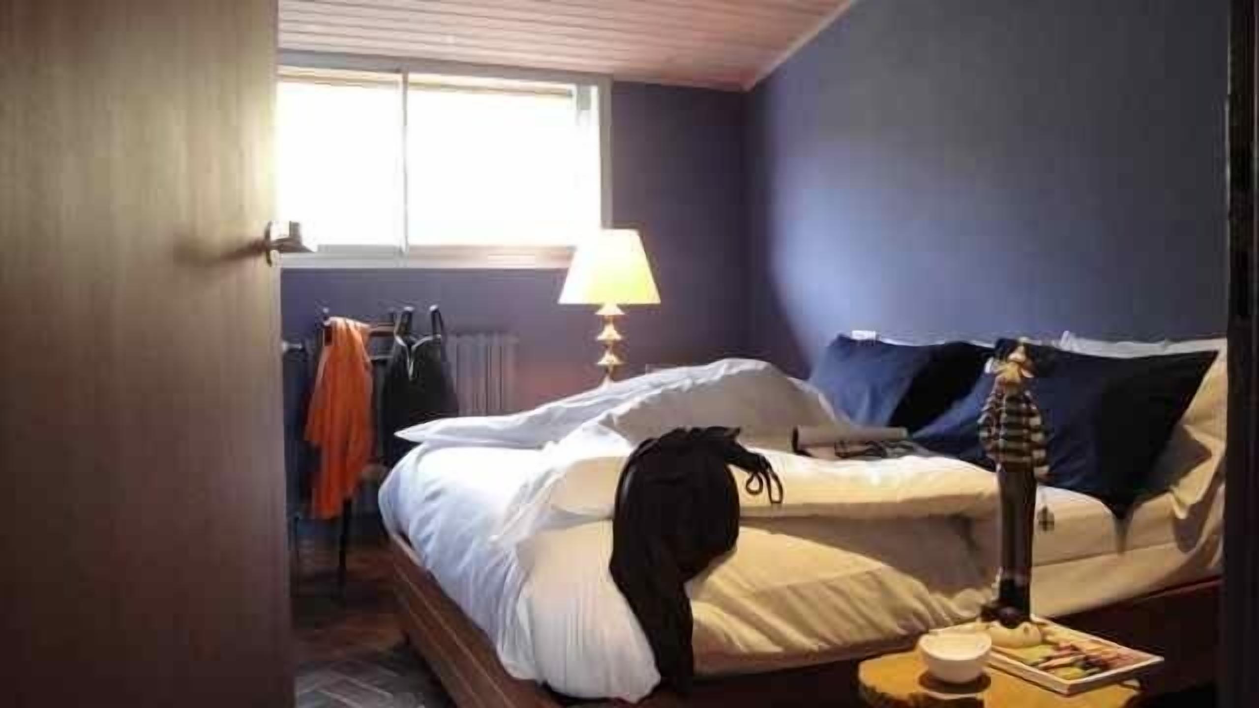 Un dormitorio con cama, lámpara, ventana y radiador.