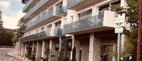A multi-story hotel with balconies, a parking area, and numbered doors.