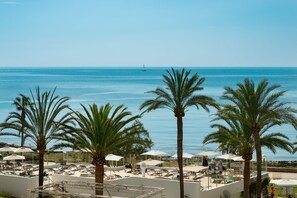 A rooftop terrace with palm trees, sun loungers, and umbrellas overlooking the sea.
