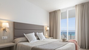 A hotel room with a large bed, two bedside lamps, a nightstand, a hat, and a view of the ocean through a balcony. - Palia Sa Coma Playa (Sant Llorenc des Cardassar)