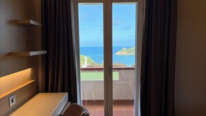 A room with a desk, chair, and a view of the sea through a glass door.