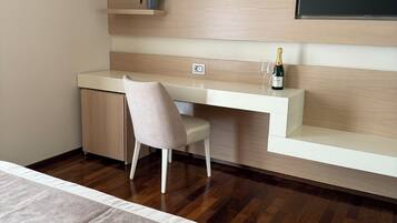 A modern bedroom with a bed, a desk, a chair, a TV, and a small shelf with a plant.