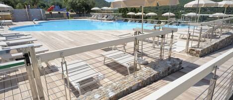 A pool area with lounge chairs and umbrellas, surrounded by stone walls and a wooden deck.