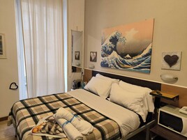 A hotel room with a bed, a painting of a wave, a heart-shaped decoration, and a nightstand with a phone.