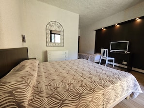 Un dormitorio con una cama grande, un aparador, un televisor sobre un mueble bajo y un espejo en la pared.