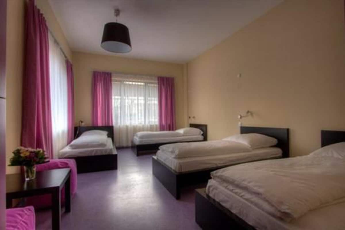 Une chambre d’hôtel avec trois lits simples, un bureau avec une chaise et une fenêtre avec des rideaux.