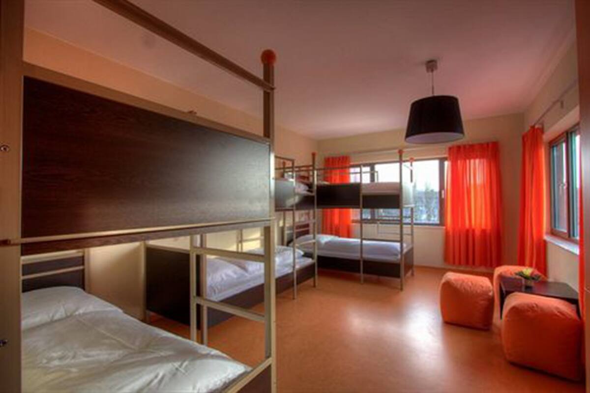 Une chambre avec des lits superposés, un luminaire suspendu et des rideaux orange.