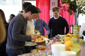 A group of people at a buffet with various food items and a red curtain in the background. - 2A Hostel (Berlin)