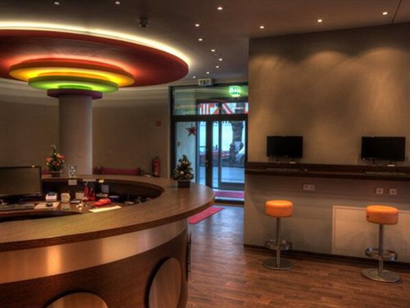 A reception area with a curved counter, two monitors, and two orange stools. - 2A Hostel (Berlin)