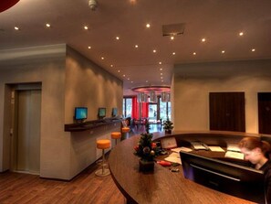 A modern hotel lobby with a curved reception desk, multiple monitors, and a piano. - 2A Hostel (Berlin)