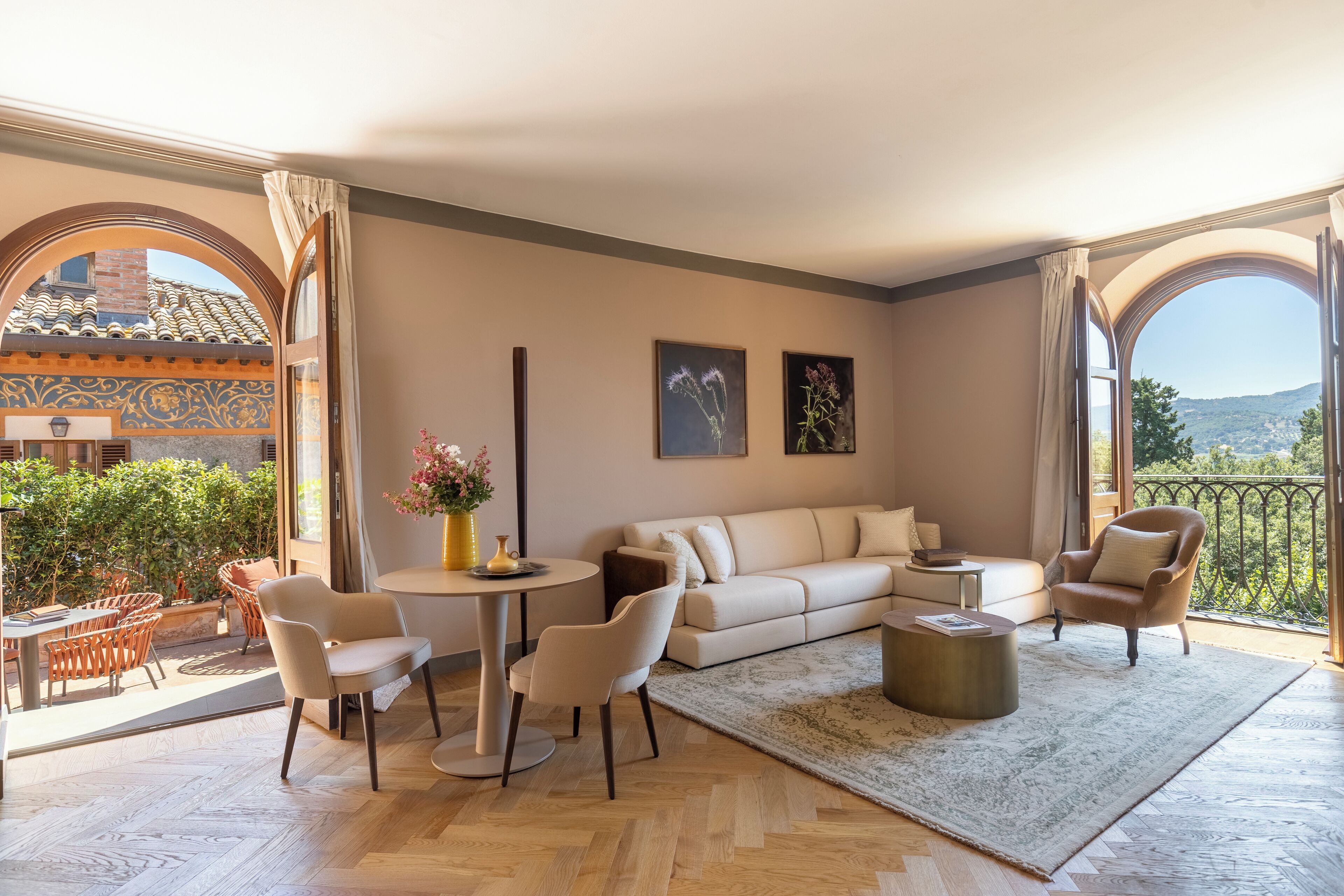 Ein geräumiges Wohnzimmer mit einem beigefarbenen Sofa, zwei Sesseln, einem Couchtisch und einem Essbereich mit Tisch und Stühlen. Große Fenster bieten einen Blick ins Freie.