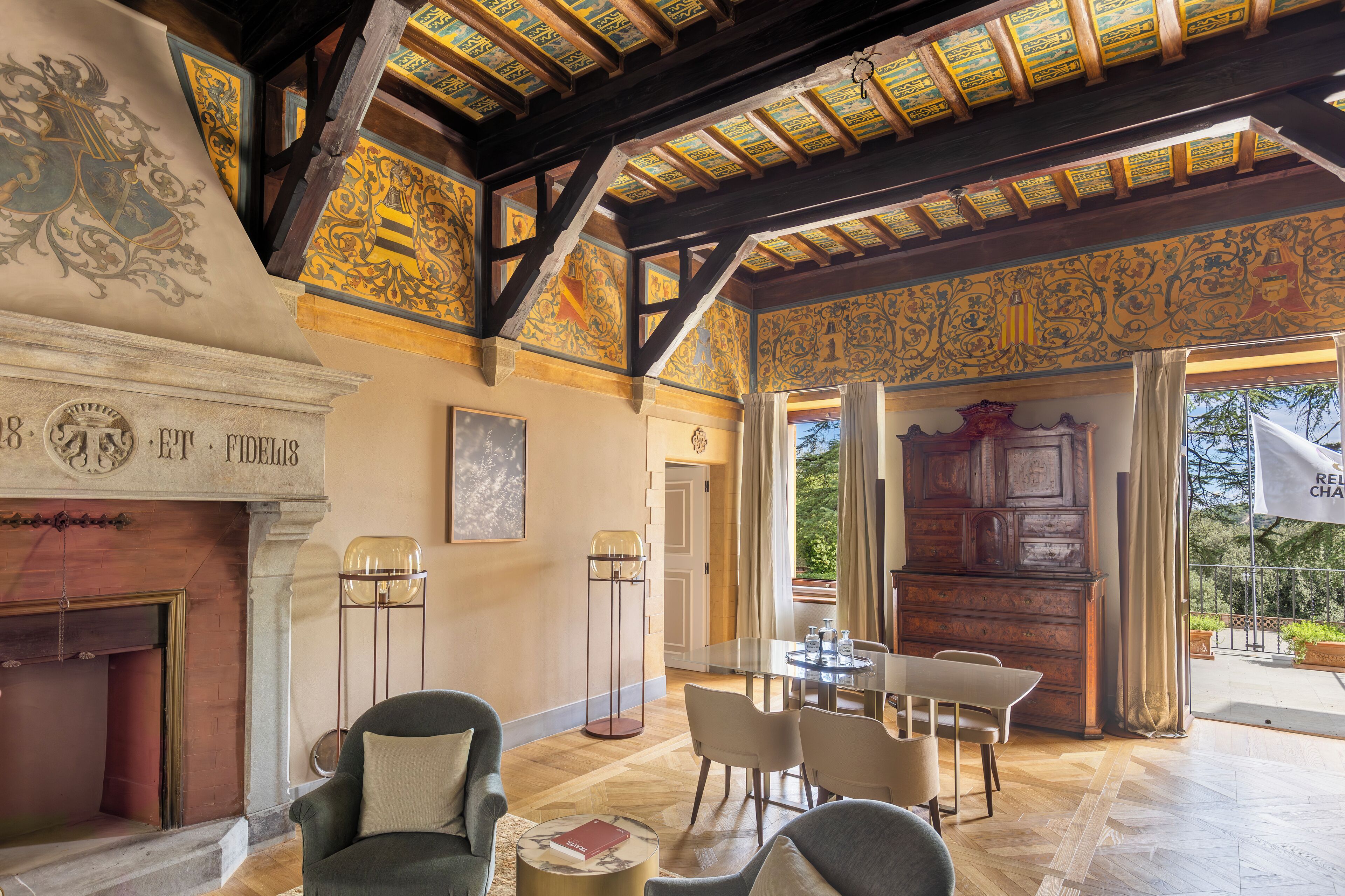 A spacious room with a high ceiling, ornate ceiling decorations, a fireplace, and a dining area with a table and chairs.