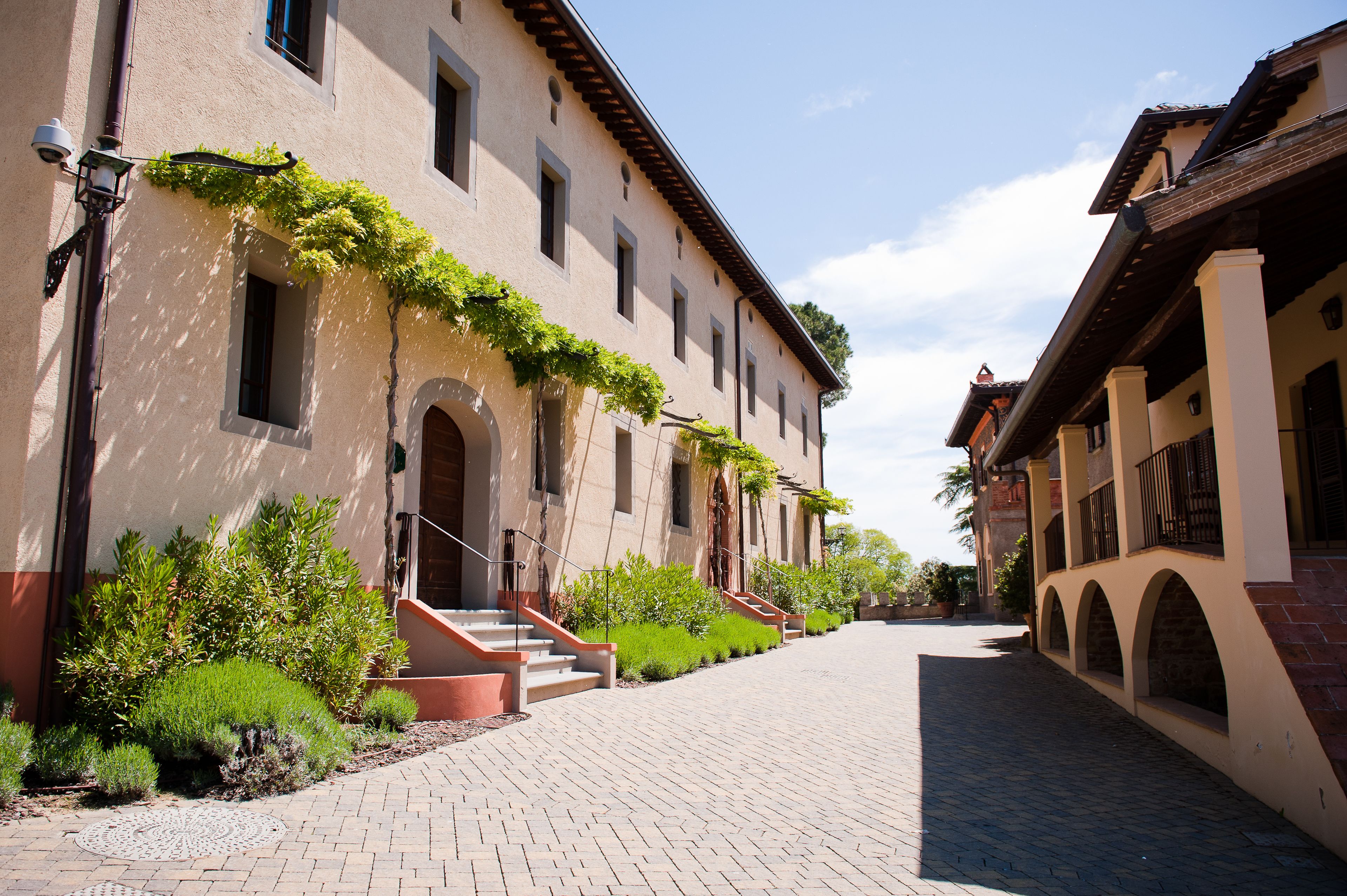 A paved courtyard with a building featuring arched windows and a staircase.