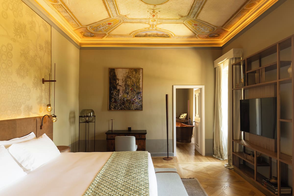 A hotel room with a large bed, a desk, a chair, a TV, and a mirror.