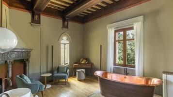 A room with a large bathtub, a fireplace, and a window with a view of greenery.